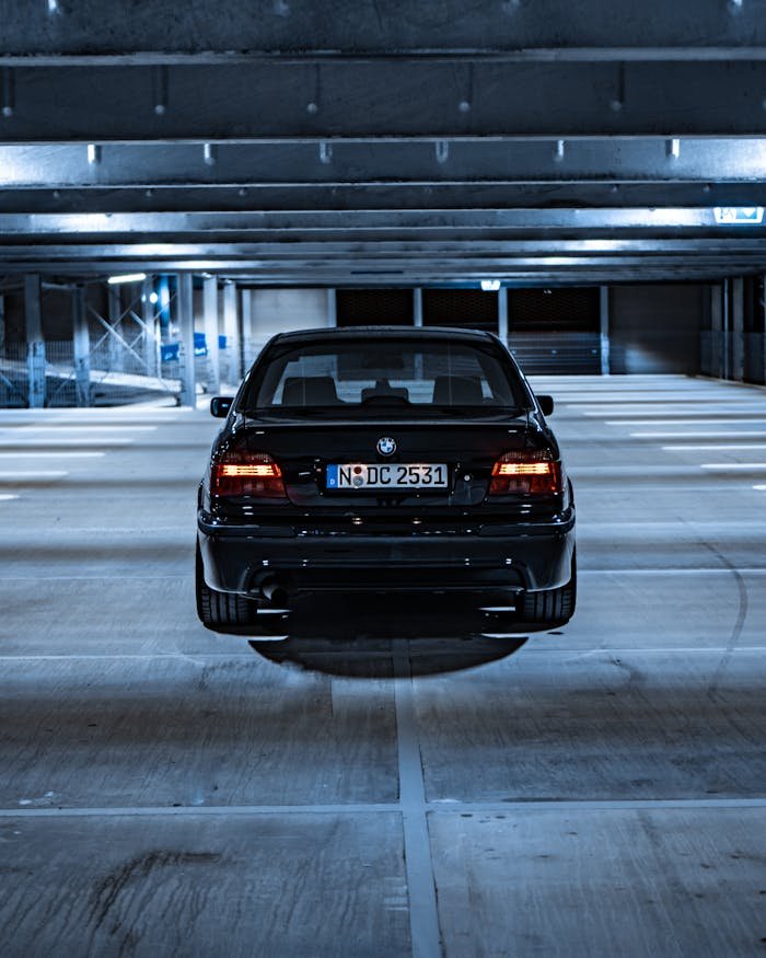 A stylish black BMW parked indoors in a modern parking garage at night with glowing tail lights.