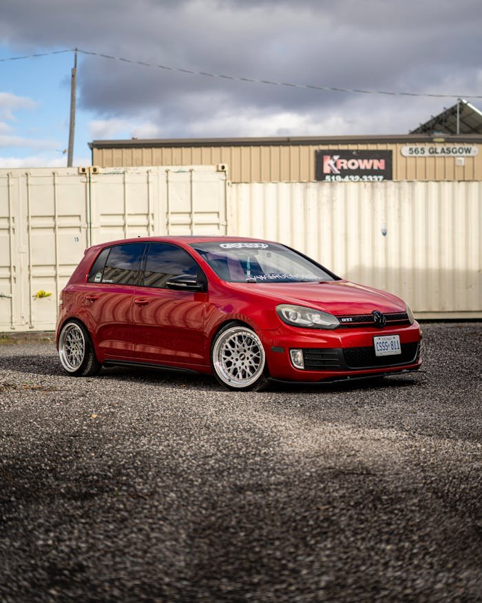 A striking red Volkswagen Golf GTI parked near industrial shipping containers in London, Canada.